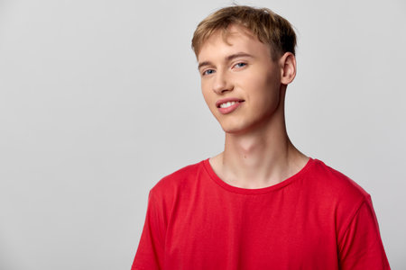 Man in a red tshirt stands in a bright studio with a relaxed smile, showcasing casual fashion, clean...