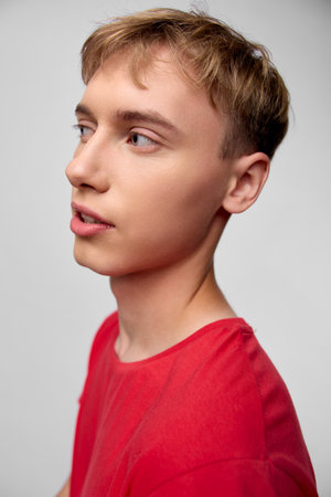 Profile of a young man in a red shirt, calm expression under studio lighting, clean neutral...