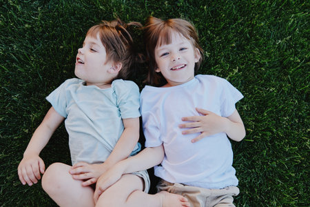 Happy children lying on grass, enjoying a sunny day with joyful expressions and playful poses,...