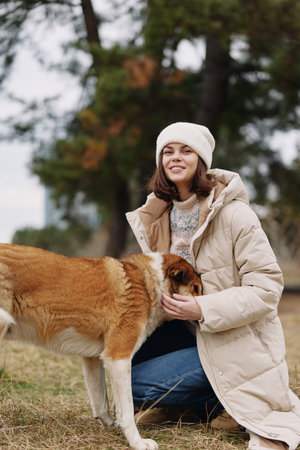 Dog and woman in an outdoor setting, wearing a warm coat and beanie, sharing a gentle moment of...