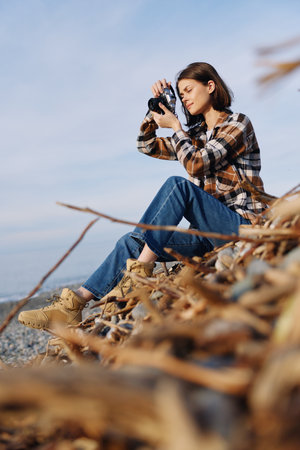 Photographer in plaid shirt captures outdoor scenery, sitting on a rocky hillside among autumn...