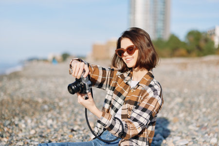 Photographer on the beach with a camera, wearing plaid shirt and sunglasses, capturing candid...