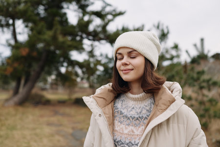 Woman outdoors in a winter coat and beanie, eyes closed in a serene moment. A peaceful portrait amid...
