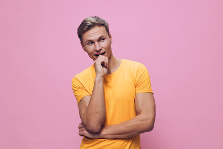 Young cheerful man with light brown hair wearing casual yellow t-shirt posing against pink...