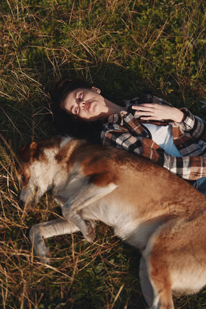 Girl and dog resting together in a sunny field, lying on grass with a joyful smile, capturing a...