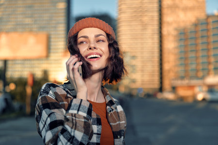 Woman on phone with smile in urban street at golden hour sunlight, candid lifestyle portrait...