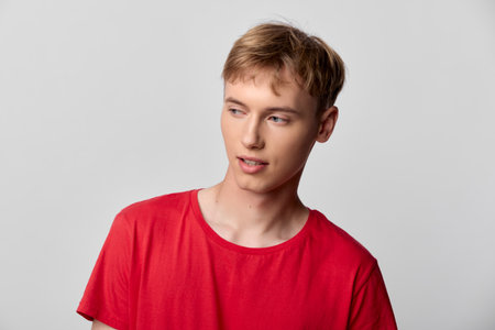 Youth, man in a casual red shirt looks away with a thoughtful expression, bright studio lighting against a clean background, contemporary everyday fashion vibeの写真素材