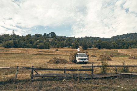 A white van rests in a wide open field beneath a cloudy sky, a weathered wooden fence in the foreground, creating a tranquil rural landscape with travel moodの写真素材