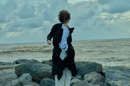 Coast scene with a coat fluttering in wind, figure on rocky shore beside a restless sea, dramatic...