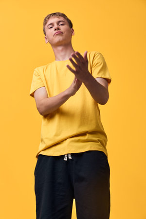 Youth in a bright yellow shirt stands against a vivid background, hands raised in a clap, conveying...