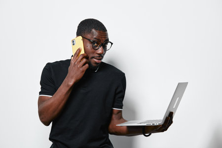 African American man with dark skin wearing glasses and black shirt talking on phone while holding...