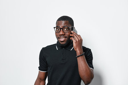 African American man with dark skin wearing glasses and black polo shirt talking on smartphone with...