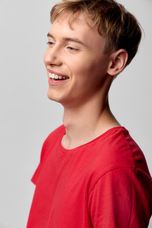 Smiling young man in a red shirt conveys happiness and confidence in a bright studio, highlighting a...