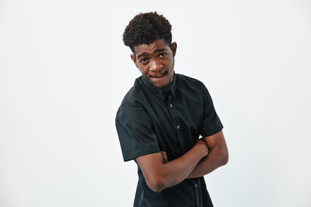 Young African American man with dark skin and curly hair wearing black shirt standing with crossed...