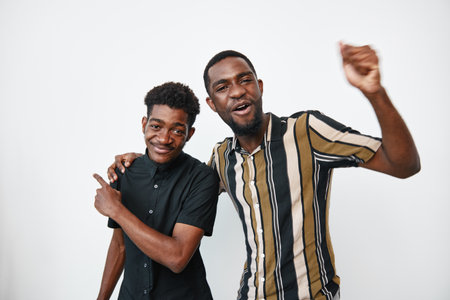Two African American men with dark skin smiling and posing together in casual clothing on white...