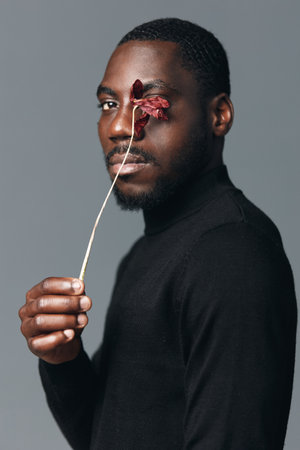 African man with dark skin holding dried flower near face in creative conceptual visual style....