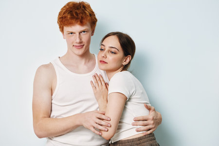 Couple, young man and woman hugging closely with emotional expression in casual white clothing on light background in studio. Relationship and affection.の写真素材