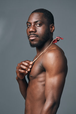 African man with dark skin and muscular body posing shirtless with creative conceptual style on gray background. Portrait of confident male model with artistic visual expression.の写真素材