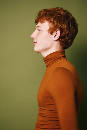 Profile portrait of young redhead man wearing brown turtleneck looking forward with neutral...