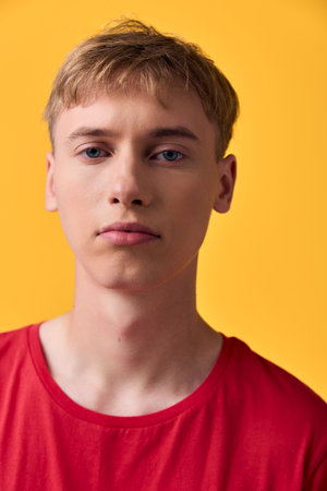 Young man with a calm expression against a bright yellow background wearing a red shirt in a close up shot with studio lighting and clean backdrop emphasizing color and moodの写真素材