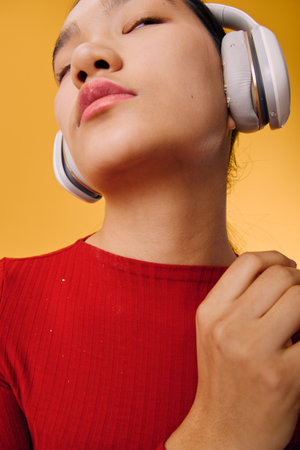 Woman wearing wireless headphones in red sweater listening to music with closed eyes, enjoying sound and relaxing on vibrant yellow background, closeup portrait of calm person.の写真素材