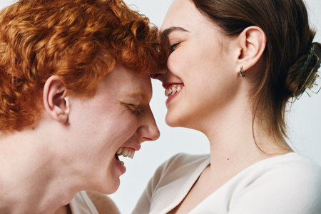 Young couple with close faces laughing and enjoying tender moment, smiling woman and man with red hair in casual clothes on white background expressing happiness and love.の写真素材