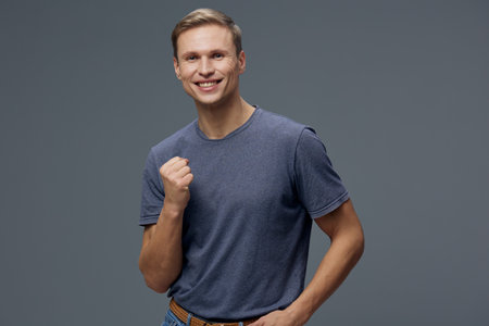 happy man wearing casual blue t-shirt smiling fist pump gesture show success isolated on grey...