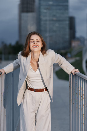 smiling woman in light beige suit laughing outdoors near city buildings, casual fashion style,...