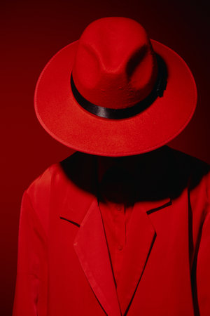 Person dressed in all red fashion attire with wide brim hat shadows face against red backdrop. Creative beauty concept focusing on bold color and dramatic style.の写真素材