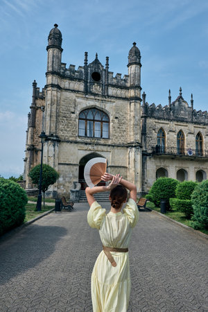 Tourist woman in a pale dress walks toward a grand castle like structure with ornate towers...