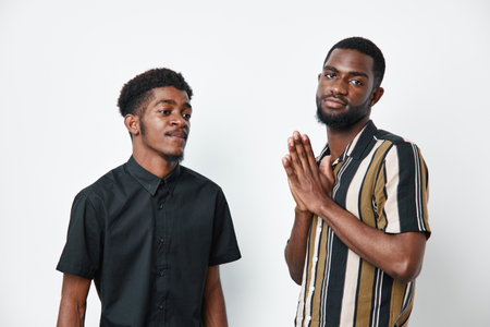 Two African American men with dark skin posing on white background, one wearing black shirt and the other striped shirt, showing casual style and confident expressions.の写真素材