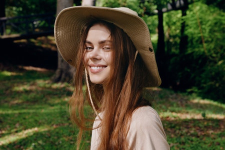 Woman smile hat portrait nature outdoors: young woman wearing a wide brim sunhat, smiling in a sunlit park with long hair and casual style for summer lifestyle and outdoor portrait.の写真素材