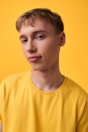 Young man in a bright yellow shirt poses casually against a vivid yellow backdrop, studio lighting creates a clean minimalist fashion image suitable for lifestyle or promotional use with a calm,の写真素材
