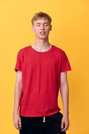 Red shirt youth in a casual studio setup against a bright yellow backdrop, relaxed pose with closed eyes, showcasing bold color, simple everyday fashion and contemporary styleの写真素材
