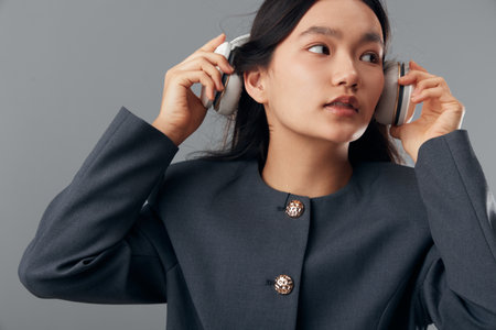 Woman, headphones, listening and fashion with gray jacket against background. Young adult female,...