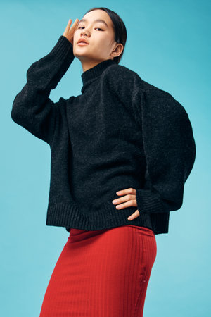 Woman posing in stylish black sweater and red skirt against blue background with confident...