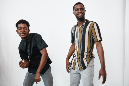 Two young black men with dark skin posing and smiling in casual clothes against white background. Male friends, fashion, lifestyle and happiness in studio portrait.の写真素材