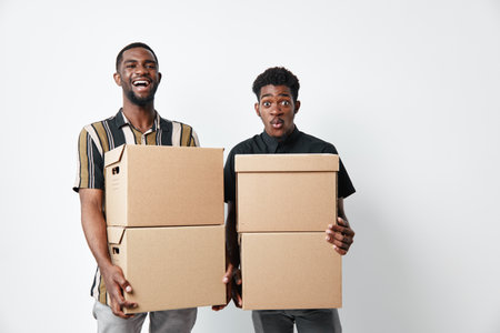 Two young black men with dark skin holding cardboard boxes for moving or delivery. African ethnicity, casual clothing, isolated on white background with happy and surprised expressions.の写真素材