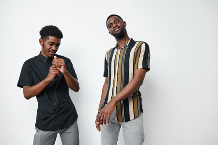 Two young black men with dark skin standing and posing in casual clothes against white background. African ethnicity, smiling and relaxed in studio portrait.の写真素材