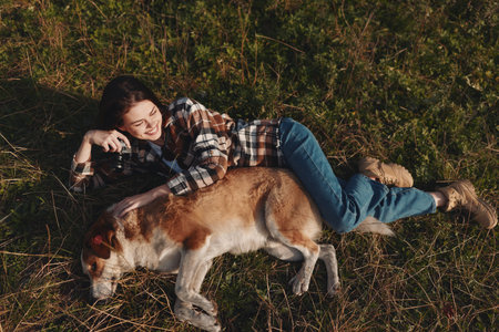 Woman lying on grass with a dog, camera in hand, capturing a candid outdoor moment during leisure...