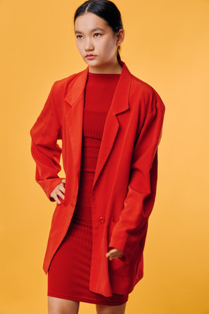 Woman wearing red oversized blazer and matching dress posing with hand on hip against yellow background. Fashion model with sleek hairstyle and confident expression in studio lighting.の写真素材
