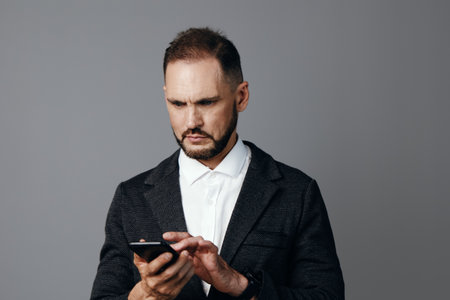 A business professional man in a dark blazer and white shirt stands before a neutral background,...