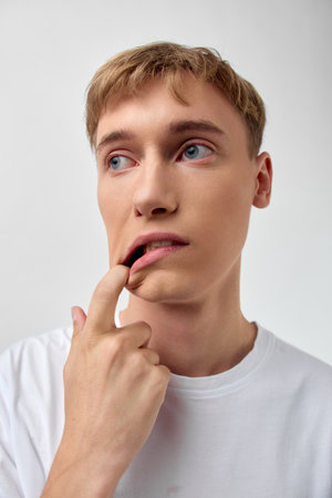 Thinking man touching lips in a white tee, pensive expression and close up mood, conveying...