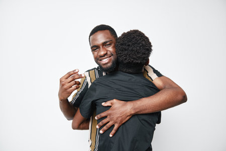 Two African American men hugging and smiling with dark skin and casual clothes on white background for friendship and connection. Happy black men embracing each other.の写真素材