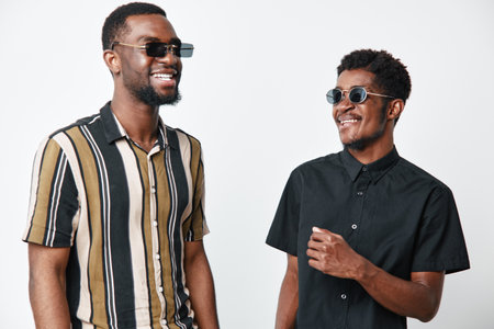 Two African American men with dark skin wearing sunglasses smiling and standing together in casual...