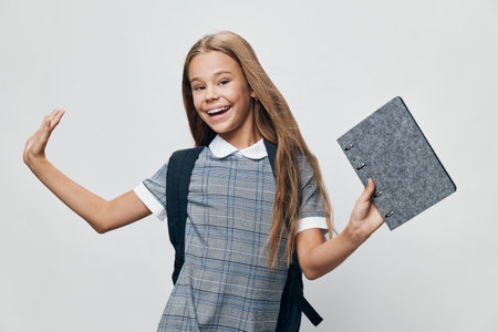 Girl student with backpack holding notebook smiling and waving hand in casual clothes on gray background for education and school concept.の写真素材