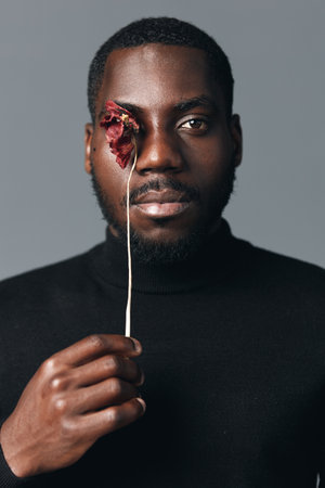 African man with dark skin holding dried flower in front of one eye in creative conceptual visual...