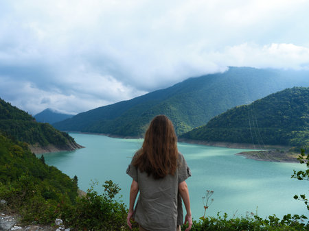 woman at viewpoint overlooking a turquoise lake and layered mountains, landscape and nature scene...