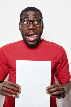African American man with dark skin wearing glasses and red sweater holding blank white paper with...