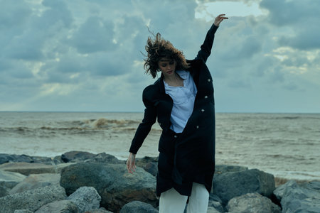 Fashion, motion, sea, wind, on rocky shoreline, a coat and white shirt move with the breeze as a...